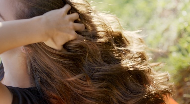 Eine Frau fasst sich in ihre langen welligen braunen Haare