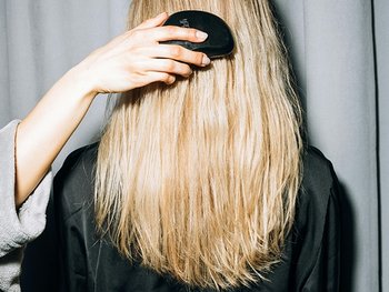 Hinterkopf einer blonden Frau, die ihre Haare gebürstet bekommt