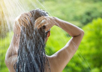 Eine Frau spült sich die Haare aus und schaut in die Natur