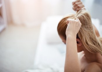 Eine Frau sitzt auf der Bettkante und macht sich einen hohen Zopf