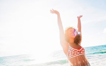 Lachende Frau am Strand, die ihre Arme in die Höhe streckt